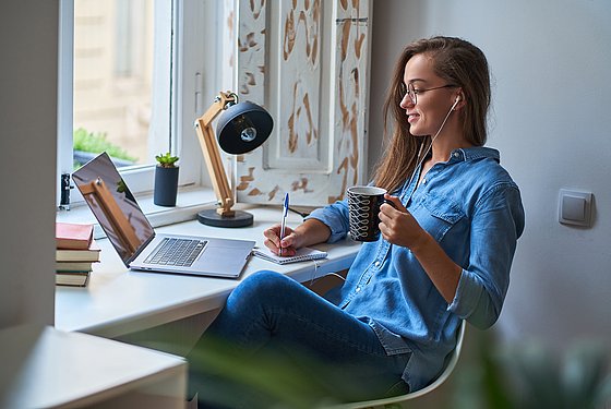 Junge Frau sitzt mit einem Kaffeebecher vor ihrem Laptop