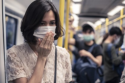 Frau in der Straßenbahn mit Gesichtsmaske hält sich die Nase