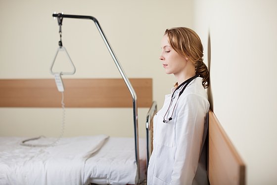 Erschöpfte Ärztin steht neben einem leeren Krankenhausbett
