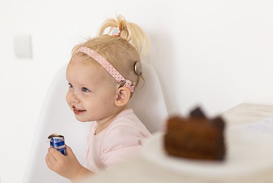 Kleines Mädchen mit einem Cochlea-Implantat isst ein Schokoladeneis