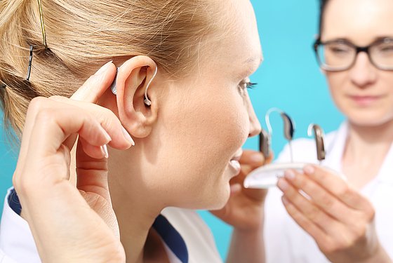 Ärztin stellt junger Frau verschiedene Hörgeräte vor
