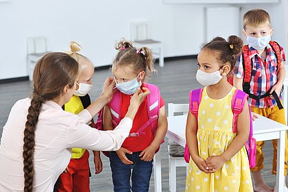 Schulkindern werden Gesichtsmasken von einer Frau zurecht gerückt.
