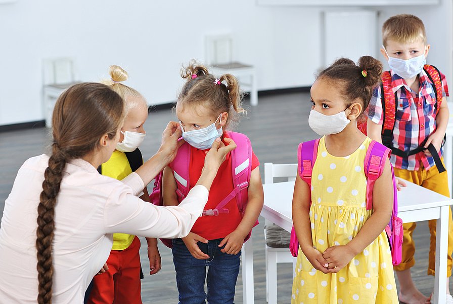 Schulkindern werden Gesichtsmasken von einer Frau zurecht gerückt.