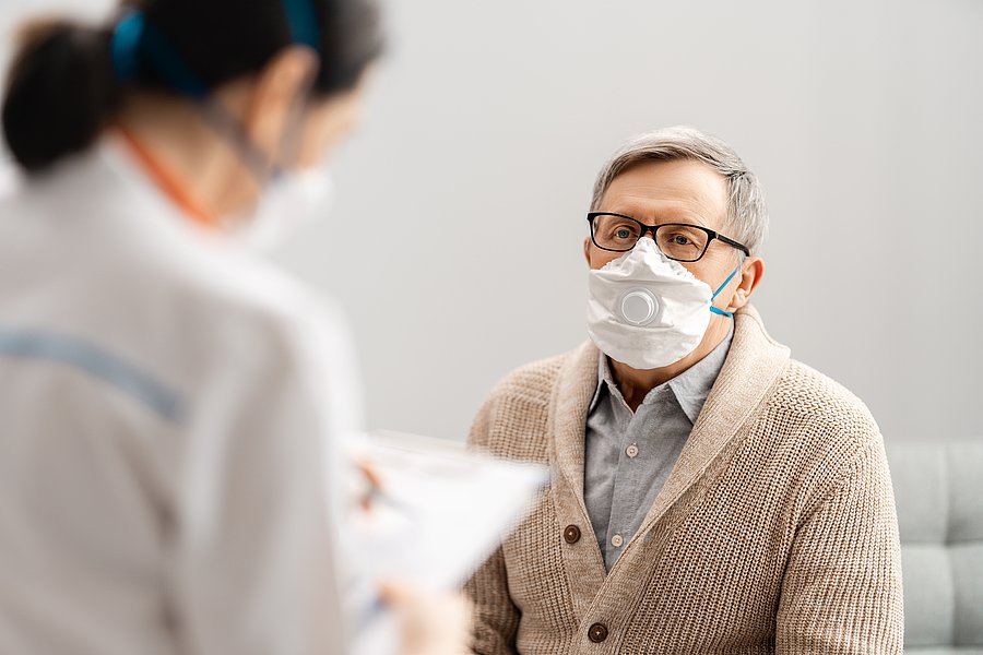 Ein Patient mit Gesichtsmaske sitzend im Gespräch mit einer Ärztin