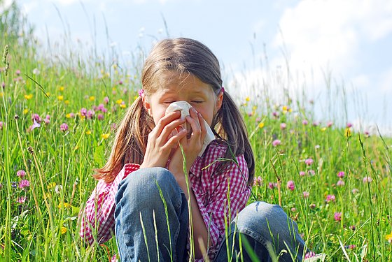 Mädchen sitzt auf einer Blumenwiese und putzt sich die Nase