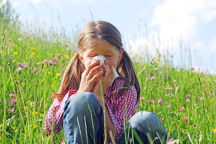 Mädchen sitzt auf einer Blumenwiese und putzt sich die Nase
