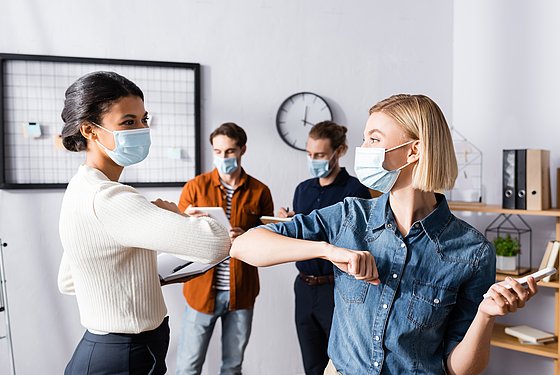 Junge Ärzte mit medizinischen Masken begrüßen sich.
